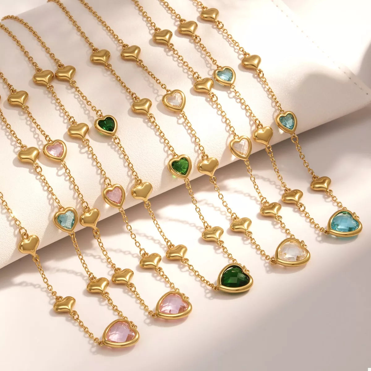 18K gold-plated heart necklace featuring a heart-shaped glass stone available in dark green, light blue, and blush pink with delicate gold heart accents.