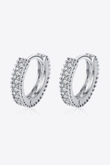 Pair of polished 925 sterling silver huggie hoop earrings featuring round inlaid moissanite stones, displayed on a soft peach background.