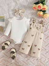 Baby girl three-piece outfit featuring a cream ribbed long-sleeve bodysuit with ruffled shoulders, apricot color bow-embroidered overalls and matching apricot bow headband.