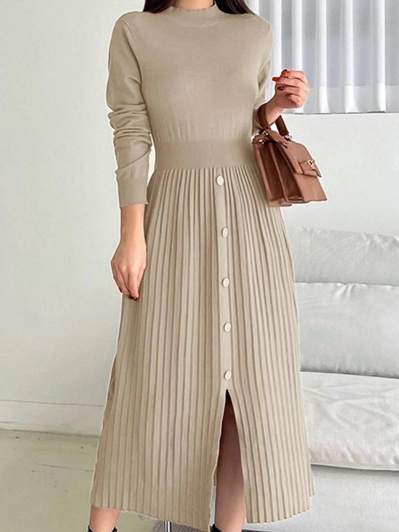 Woman wearing an apricot mock neck long sleeve knit midi dress with pleated skirt, front buttons and slit.