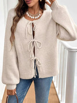 Woman wearing a apricot tie-front long sleeve knit cardigan with three bow ties paired with blue jeans.
