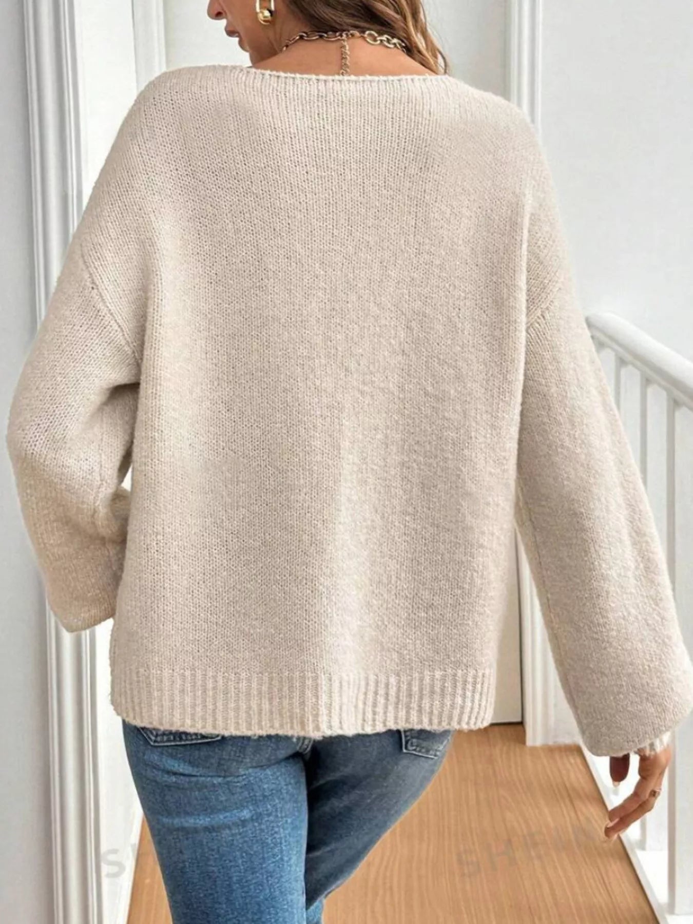 Woman wearing an apricot tie-front long sleeve knit cardigan with three bow ties paired with blue jeans.