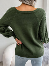 Woman wearing an army green cable-knit sweater with decorative buttons, paired with light-wash jeans, layered gold necklaces, and a white handbag. Perfect for cozy fall and winter outfits.
