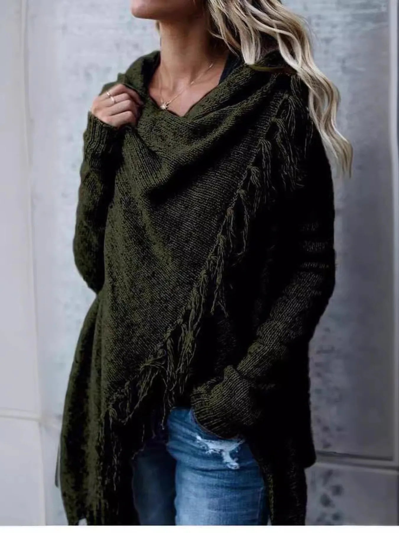 Woman wearing an army green fringe long sleeve wrap cardigan with an asymmetrical draped front over a white top and jeans.