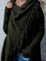 Woman wearing an army green fringe long sleeve wrap cardigan with an asymmetrical draped front over a white top and jeans.