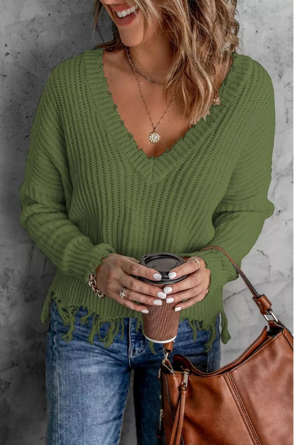 Woman wearing an army green ribbed V-neck sweater with distressed raw hem and blue jeans.