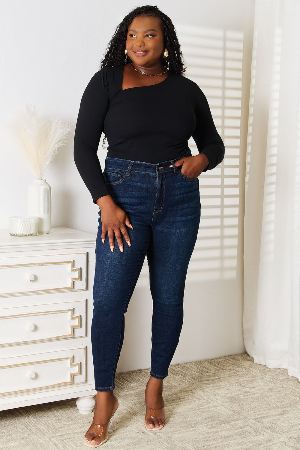 Woman wearing a black Basic Bae asymmetrical neck long-sleeve top paired with dark-wash jeans, creating a chic and modern look.