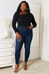 Woman wearing a black Basic Bae asymmetrical neck long-sleeve top paired with dark-wash jeans, creating a chic and modern look.