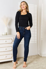 Woman wearing a black Basic Bae asymmetrical neck long-sleeve top paired with dark-wash jeans, creating a chic and modern look.