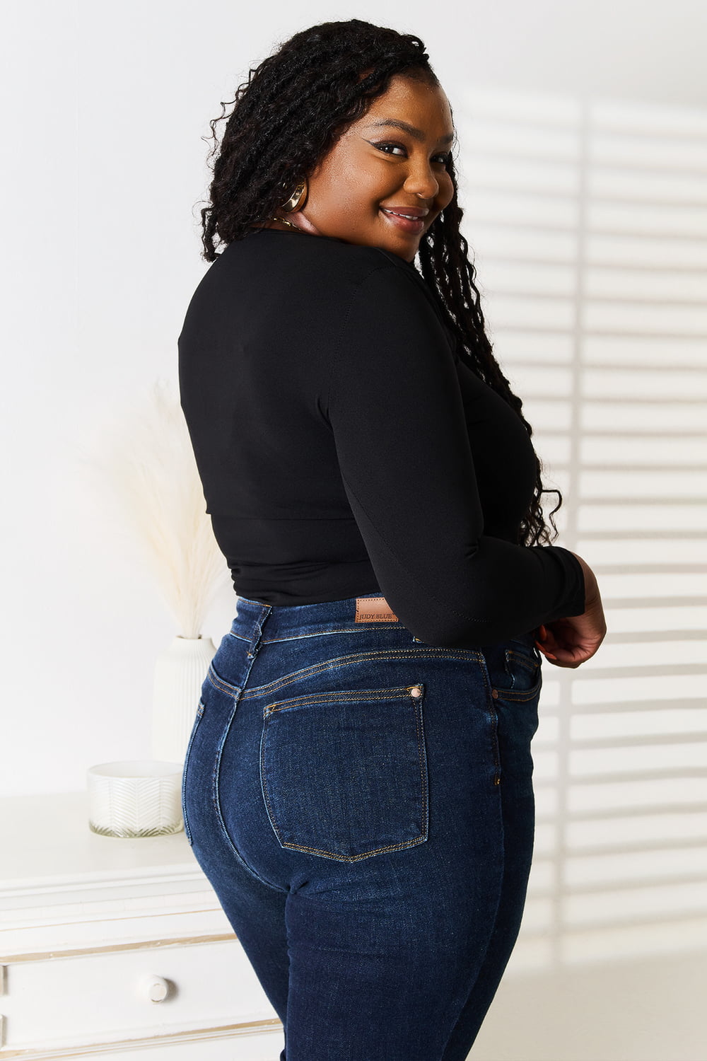 Woman wearing a black Basic Bae asymmetrical neck long-sleeve top paired with dark-wash jeans, creating a chic and modern look.