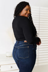 Woman wearing a black Basic Bae asymmetrical neck long-sleeve top paired with dark-wash jeans, creating a chic and modern look.