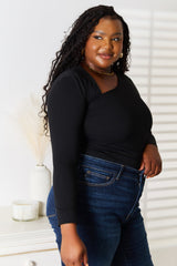 Woman wearing a black Basic Bae asymmetrical neck long-sleeve top paired with dark-wash jeans, creating a chic and modern look.