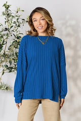 Woman wearing a blue ribbed long sleeve knit top with a round neckline and side slit detail.
