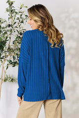 Woman wearing a blue ribbed long sleeve knit top with a round neckline and side slit detail.