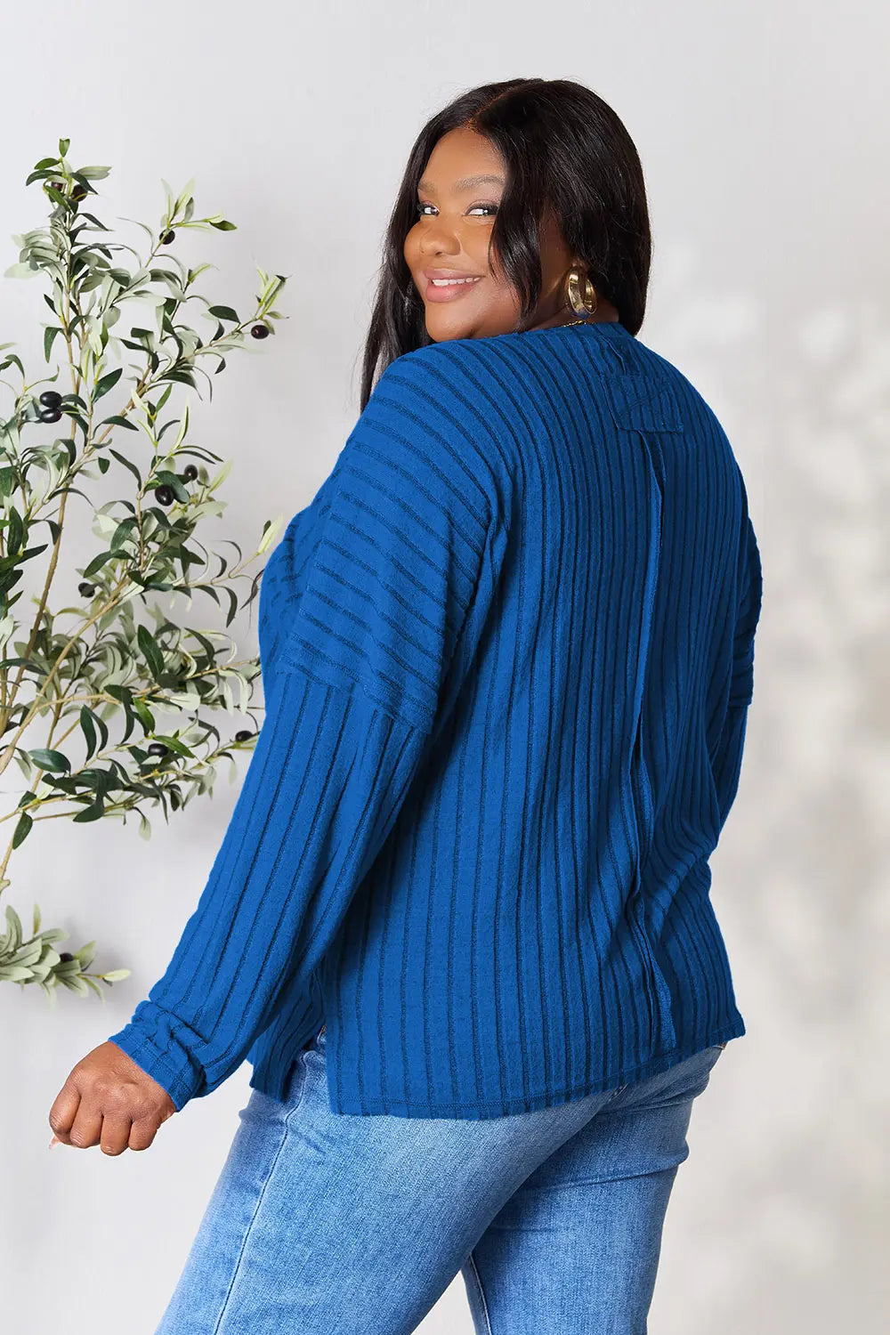 Woman wearing a blue ribbed long sleeve knit top with a round neckline and side slit detail.
