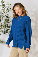 Woman wearing a blue ribbed long sleeve knit top with a round neckline and side slit detail.