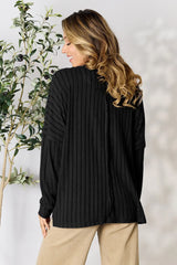 Woman wearing a black ribbed long sleeve knit top with a round neckline and side slit detail.