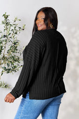 Woman wearing a black ribbed long sleeve knit top with a round neckline and side slit detail.