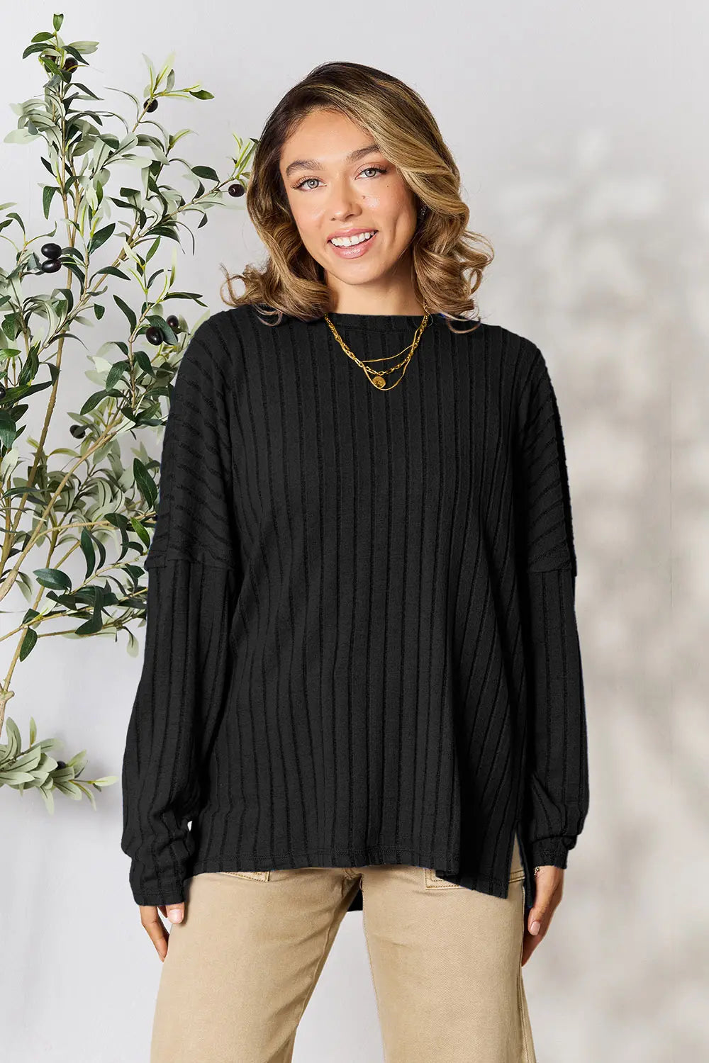 Woman wearing a black ribbed long sleeve knit top with a round neckline and side slit detail.