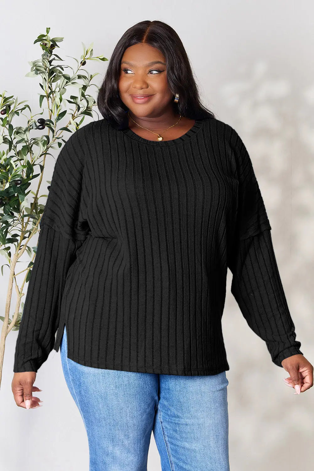 Woman wearing a black ribbed long sleeve knit top with a round neckline and side slit detail.