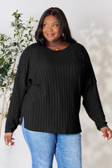 Woman wearing a black ribbed long sleeve knit top with a round neckline and side slit detail.