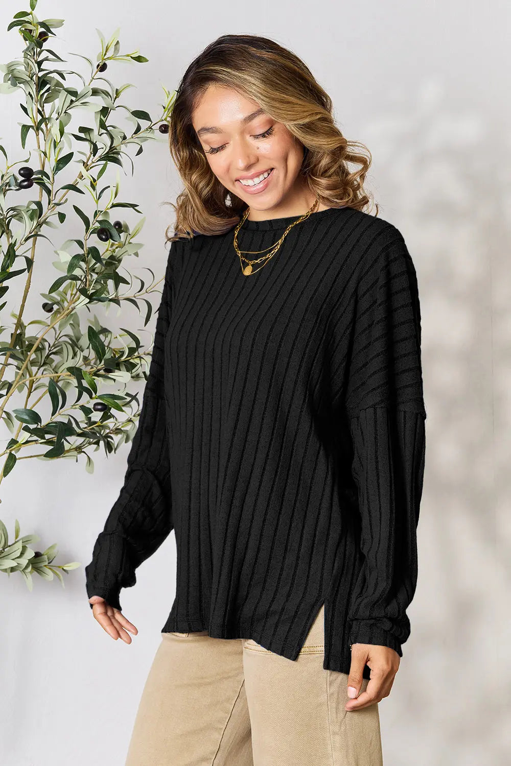 Woman wearing a black ribbed long sleeve knit top with a round neckline and side slit detail.