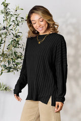 Woman wearing a black ribbed long sleeve knit top with a round neckline and side slit detail.