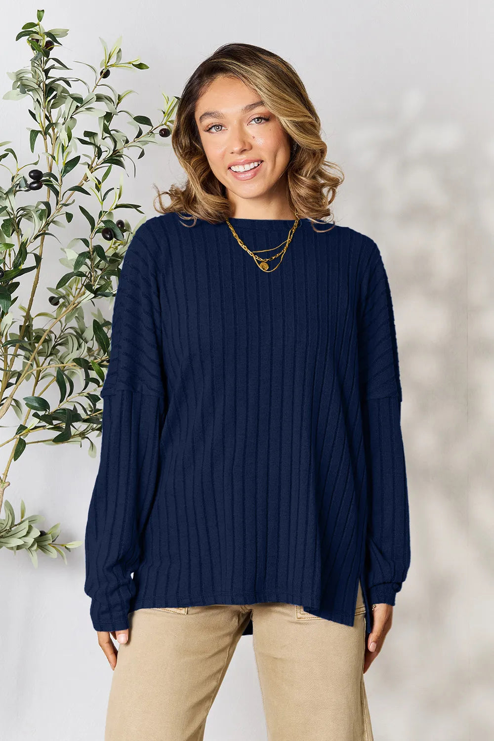 Woman wearing a dark blue ribbed long sleeve knit top with a round neckline and side slit detail.