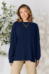 Woman wearing a dark blue ribbed long sleeve knit top with a round neckline and side slit detail.