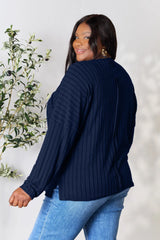 Woman wearing a dark blue ribbed long sleeve knit top with a round neckline and side slit detail.