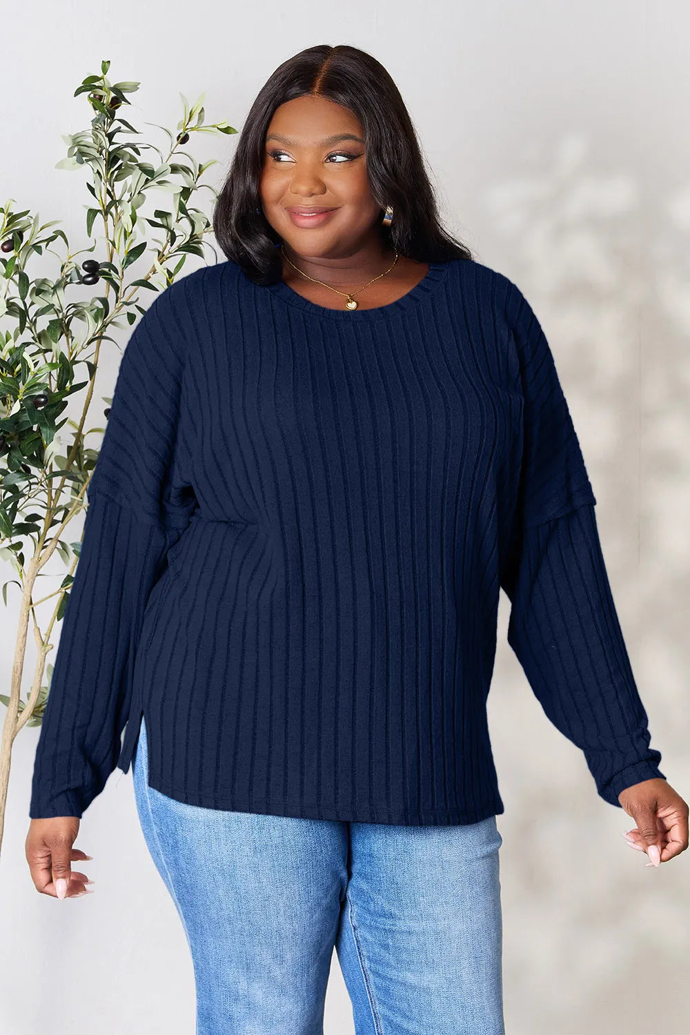 Woman wearing a dark blue ribbed long sleeve knit top with a round neckline and side slit detail.