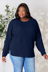 Woman wearing a dark blue ribbed long sleeve knit top with a round neckline and side slit detail.
