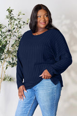 Woman wearing a dark blue ribbed long sleeve knit top with a round neckline and side slit detail.