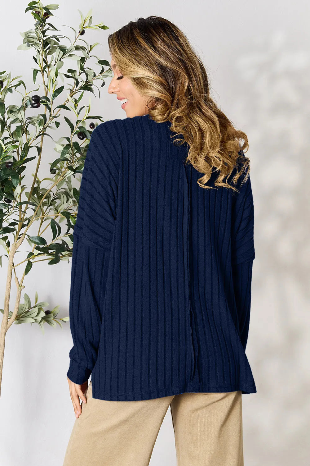 Woman wearing a dark blue ribbed long sleeve knit top with a round neckline and side slit detail.