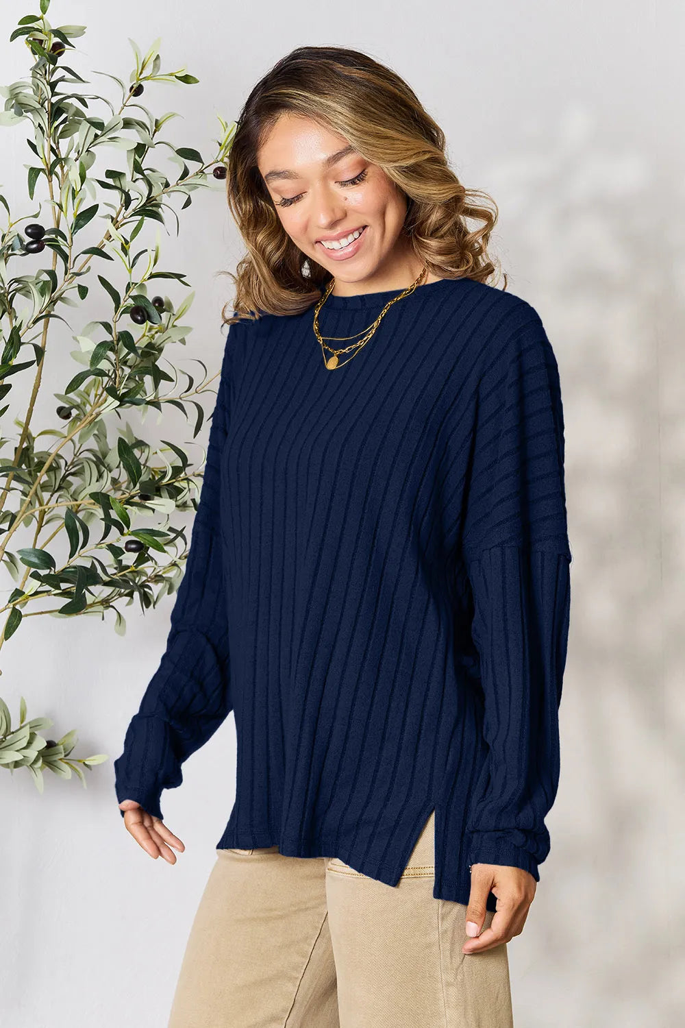 Woman wearing a dark blue ribbed long sleeve knit top with a round neckline and side slit detail.