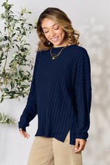 Woman wearing a dark blue ribbed long sleeve knit top with a round neckline and side slit detail.