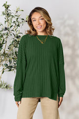 Woman wearing a dark green ribbed long sleeve knit top with a round neckline and side slit detail.