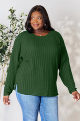 Woman wearing a dark green ribbed long sleeve knit top with a round neckline and side slit detail.
