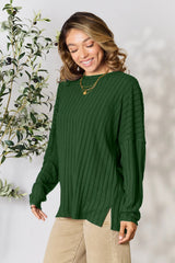 Woman wearing a dark green ribbed long sleeve knit top with a round neckline and side slit detail.