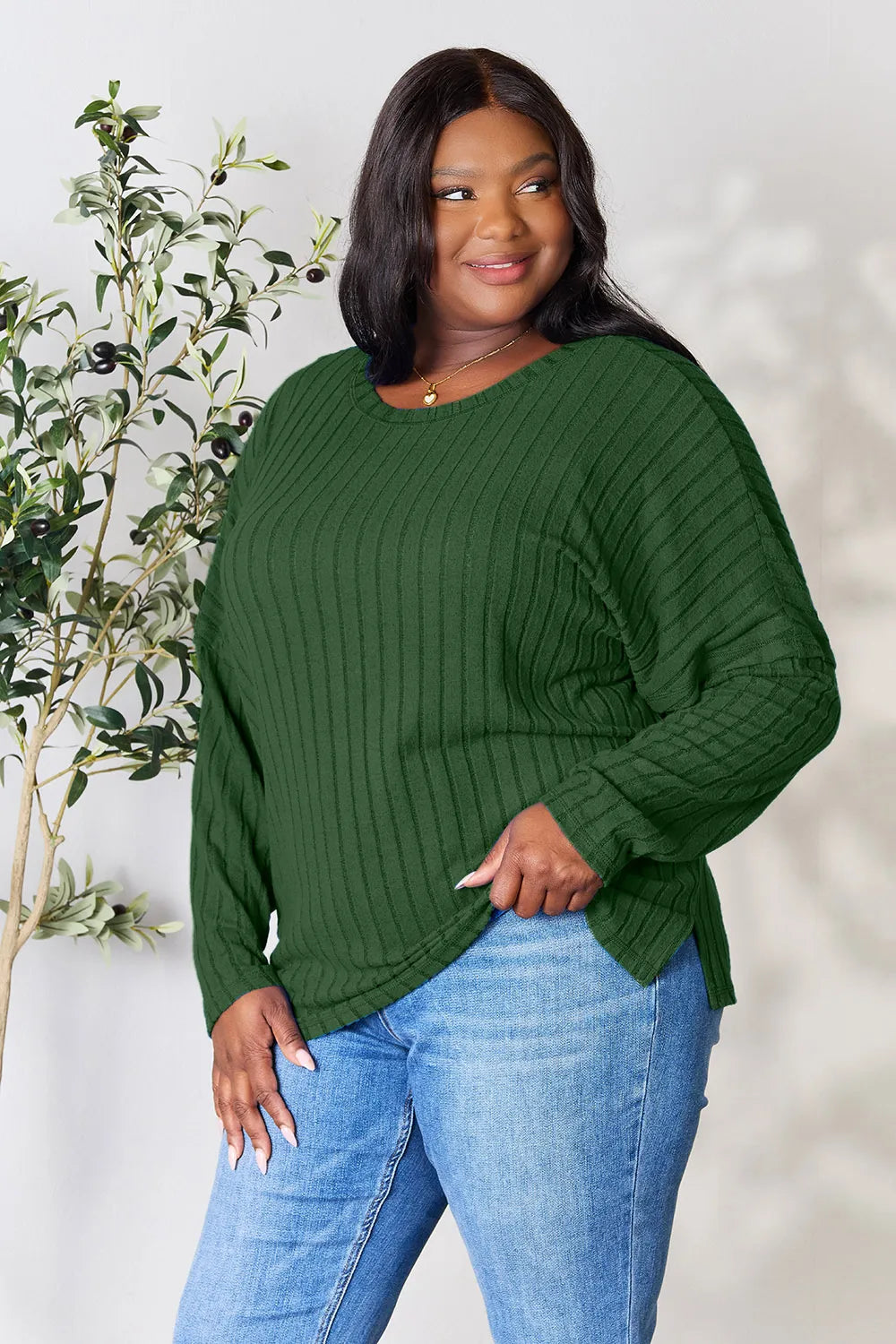 Woman wearing a dark green ribbed long sleeve knit top with a round neckline and side slit detail.