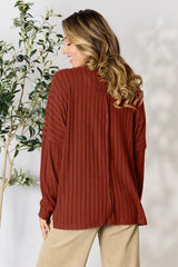 Woman wearing a rust ribbed long sleeve knit top with a round neckline and side slit detail.