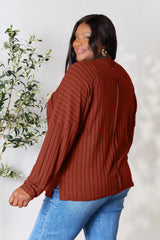 Woman wearing a rust ribbed long sleeve knit top with a round neckline and side slit detail.