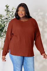 Woman wearing a rust ribbed long sleeve knit top with a round neckline and side slit detail.
