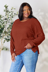 Woman wearing a rust ribbed long sleeve knit top with a round neckline and side slit detail.