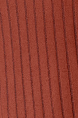 Woman wearing a rust ribbed long sleeve knit top with a round neckline and side slit detail.