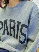 Woman wearing a light gray Basic Bae PARIS round-neck air scuba sweatshirt with long sleeves, styled with dark-wash jeans for a casual and comfortable look.