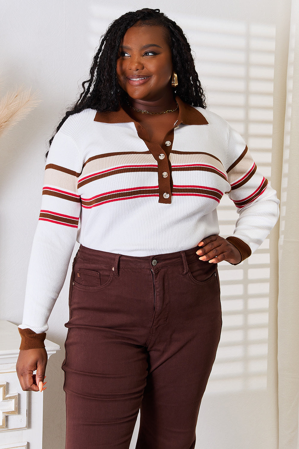 Woman wearing a white striped rib-knit top with a collared neckline and button-front detail, paired with brown jeans for a polished and sophisticated look.