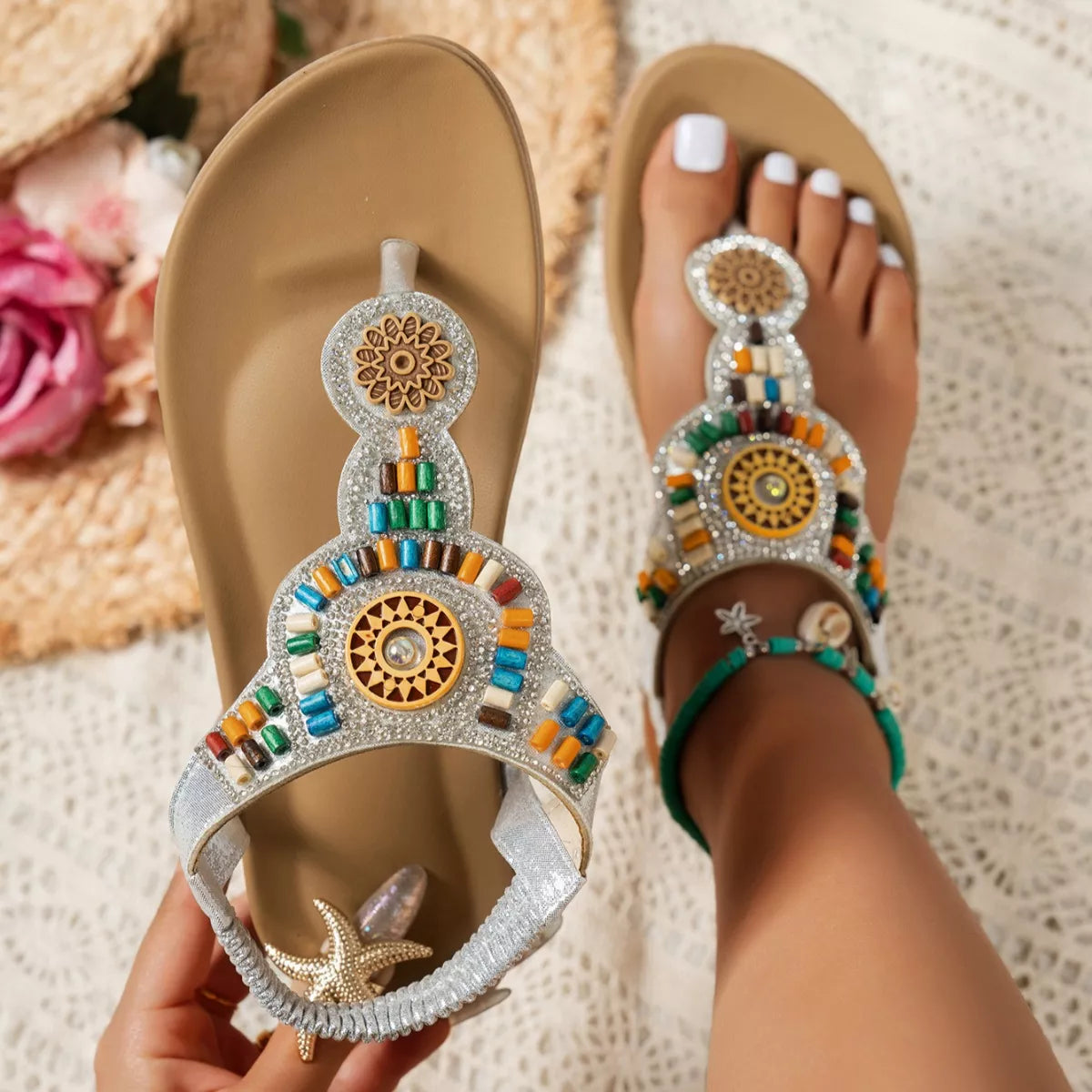 Beige sandals with colorful embellishments held by a hand on a textured surface.