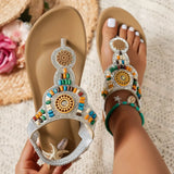 Beige sandals with colorful embellishments held by a hand on a textured surface.