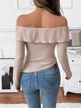 Woman wearing a beige asymmetrical off-shoulder ribbed knit top with twisted neckline and long sleeves paired with blue jeans.